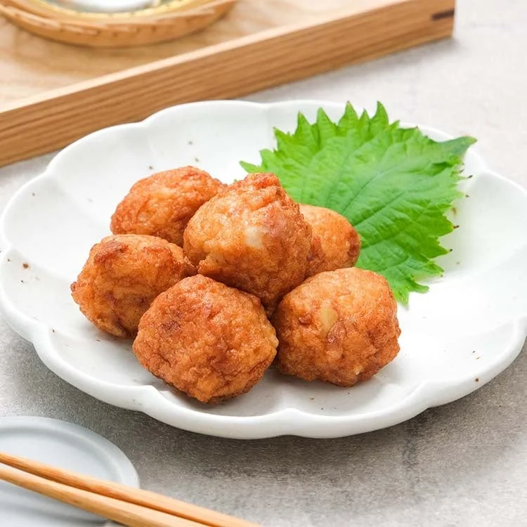 白い花形の皿に、きつね色に揚がった丸い揚げ物が数個盛り付けられています。緑鮮やかな大葉が添えられ、食欲をそそる和食のおかずのようです。