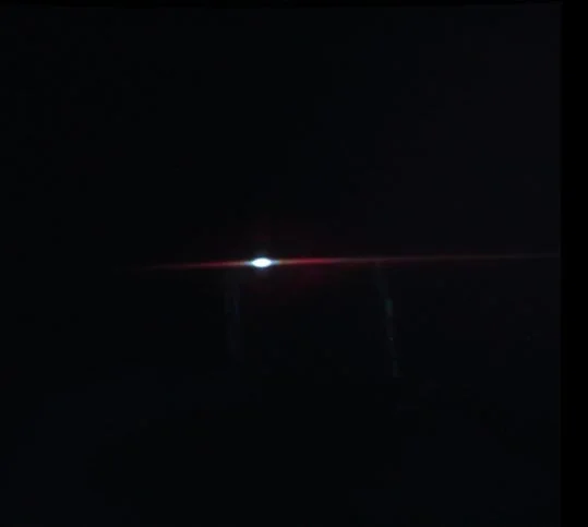 暗い背景の中央に明るい光があり、そこから赤い水平なレンズフレアが伸びています