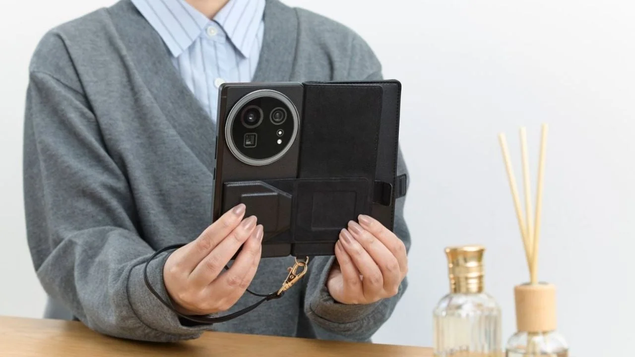 女性が大きなカメラモジュールを持つ黒いスマートフォンを、ストラップ付きのフォリオケースに入れた状態で両手で持っている様子