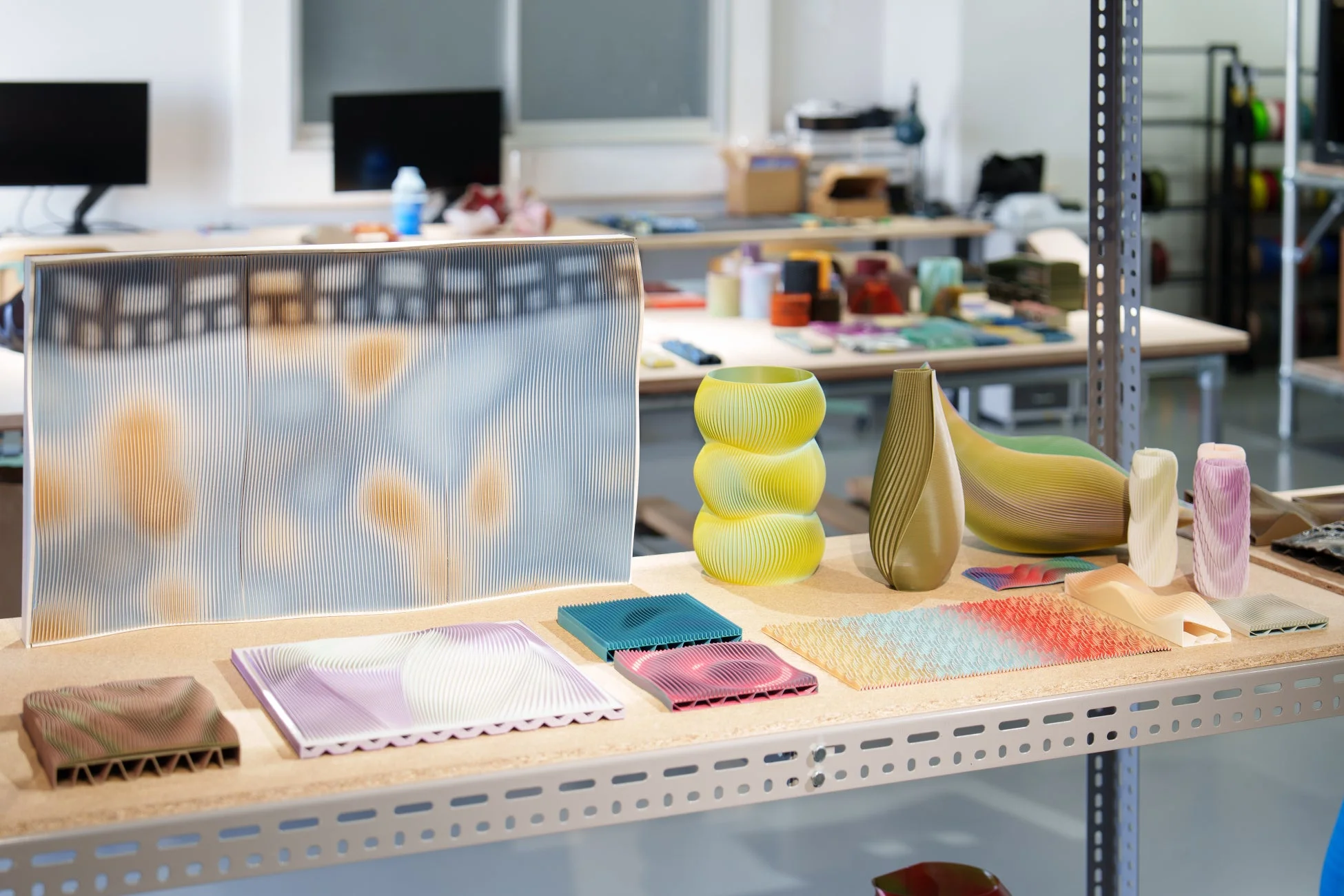 棚に並べられた、波状やリブ加工のテクスチャとグラデーションカラーが特徴的な3Dプリント作品群