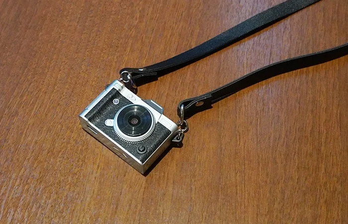 木製のテーブルの上に置かれた、レトロなデザインの小型デジタルカメラです。黒いストラップが取り付けられています。