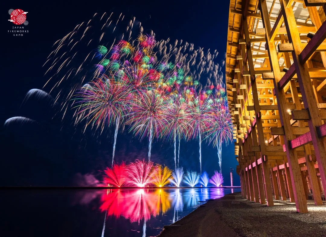 水面に反射する色とりどりの花火と木造建築