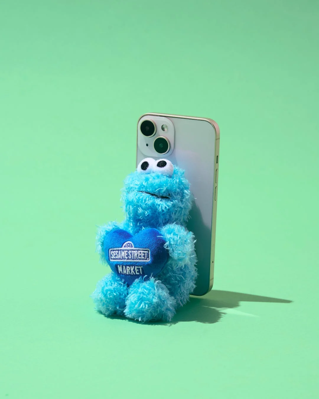 クッキーモンスターのような青いぬいぐるみが、背中にスマートフォンを立てかけている