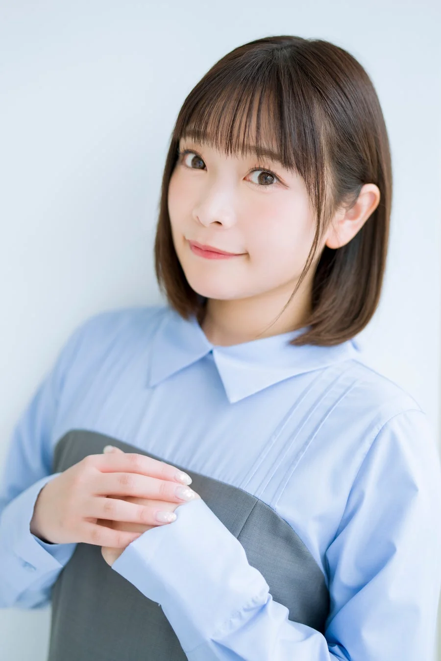 水色のシャツとグレーの服を身につけた若い日本人女性が、優しく微笑みながらカメラを見つめているポートレート