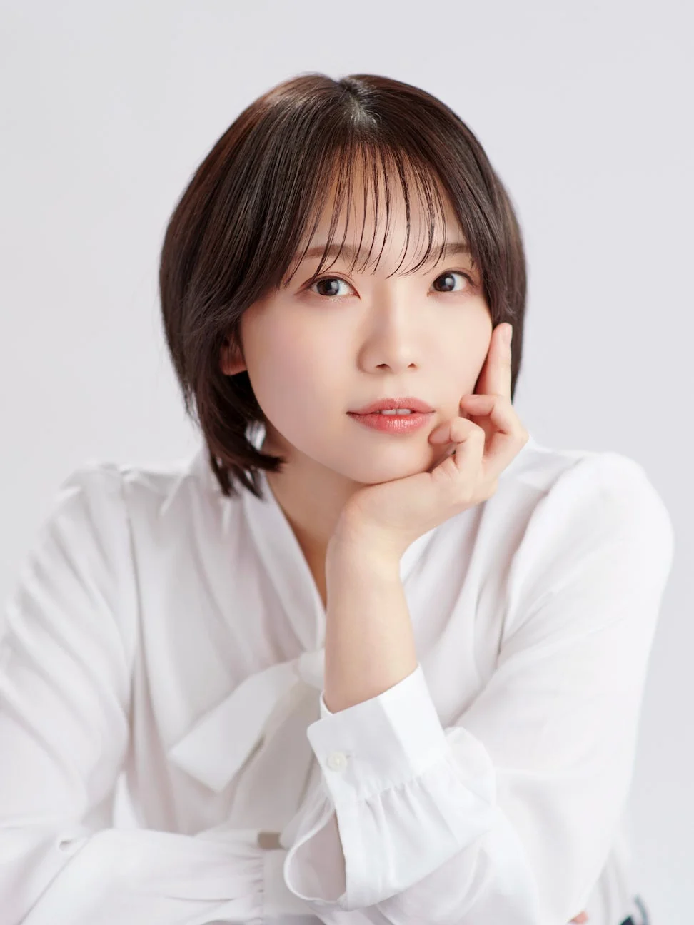 白いボウタイブラウスを着用したショートヘアのアジア人女性