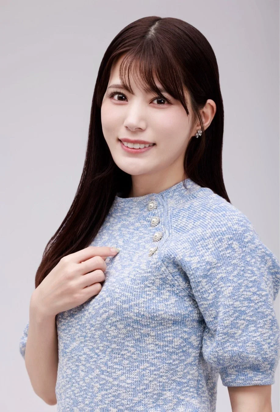 水色のニットセーターを着用し、明るい笑顔でカメラを見つめる若いアジア人女性