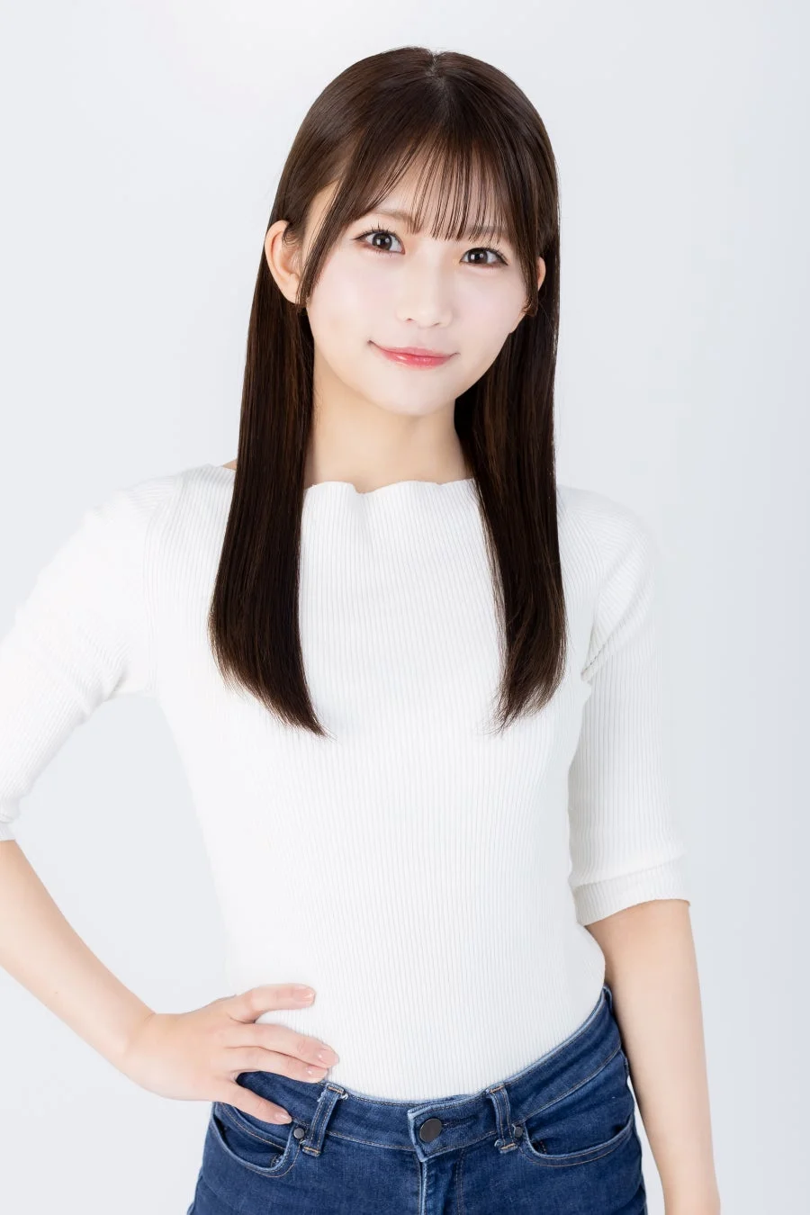 白いリブニットのトップスとジーンズを着用した若い女性