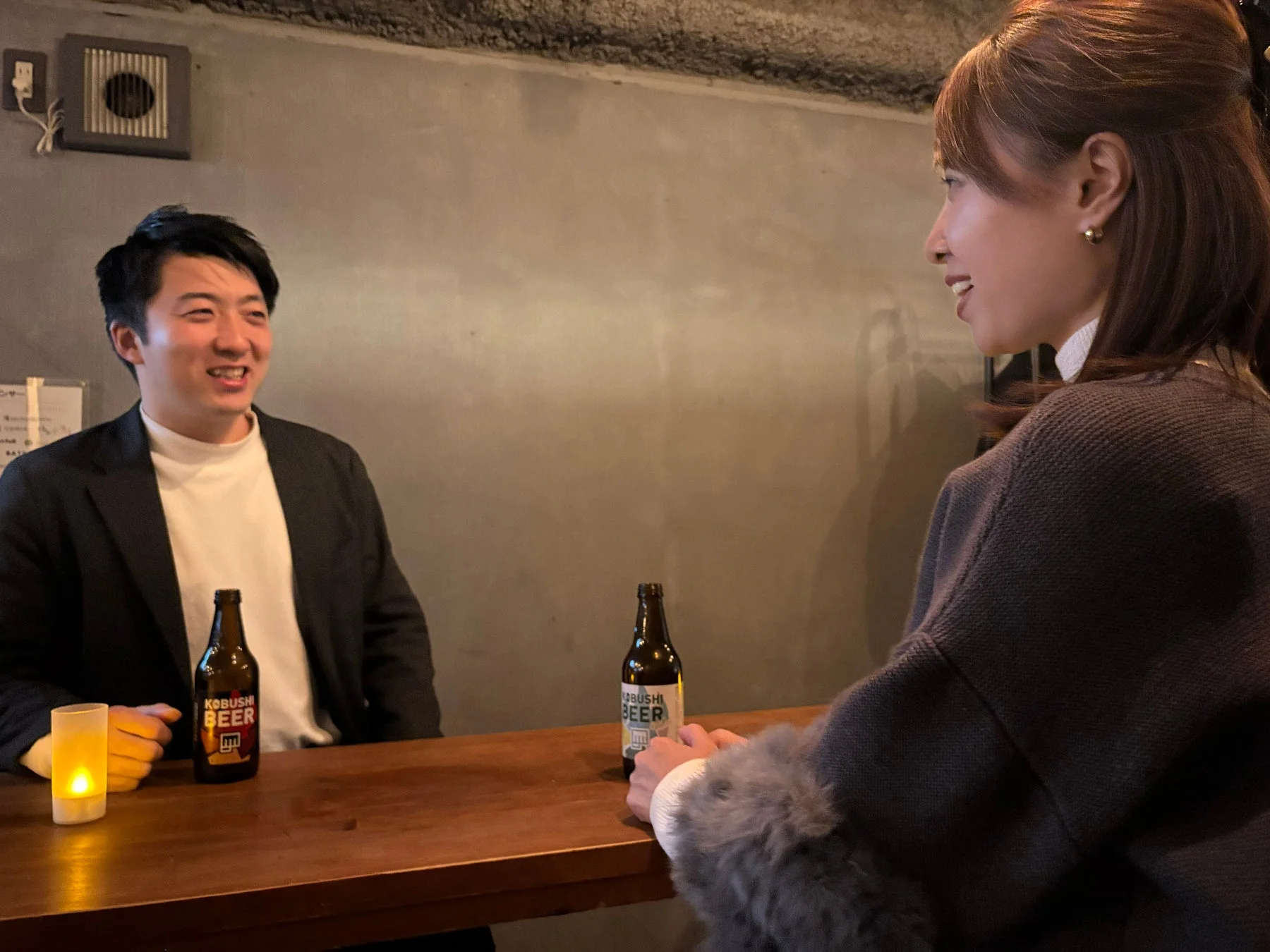 バーカウンターで男女が笑顔でビールを飲みながら会話している様子