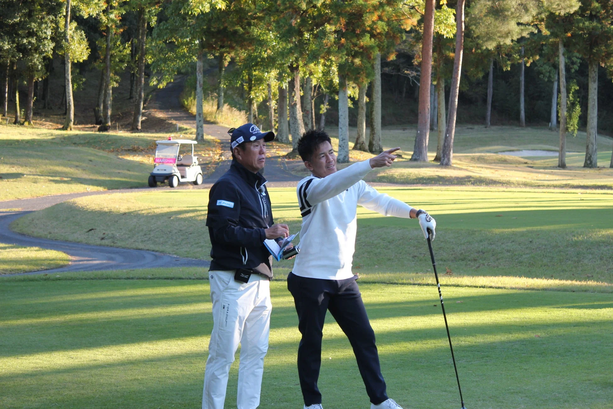 ゴルフ場で、一人の男性がゴルフクラブを持ちながら遠くを指差し