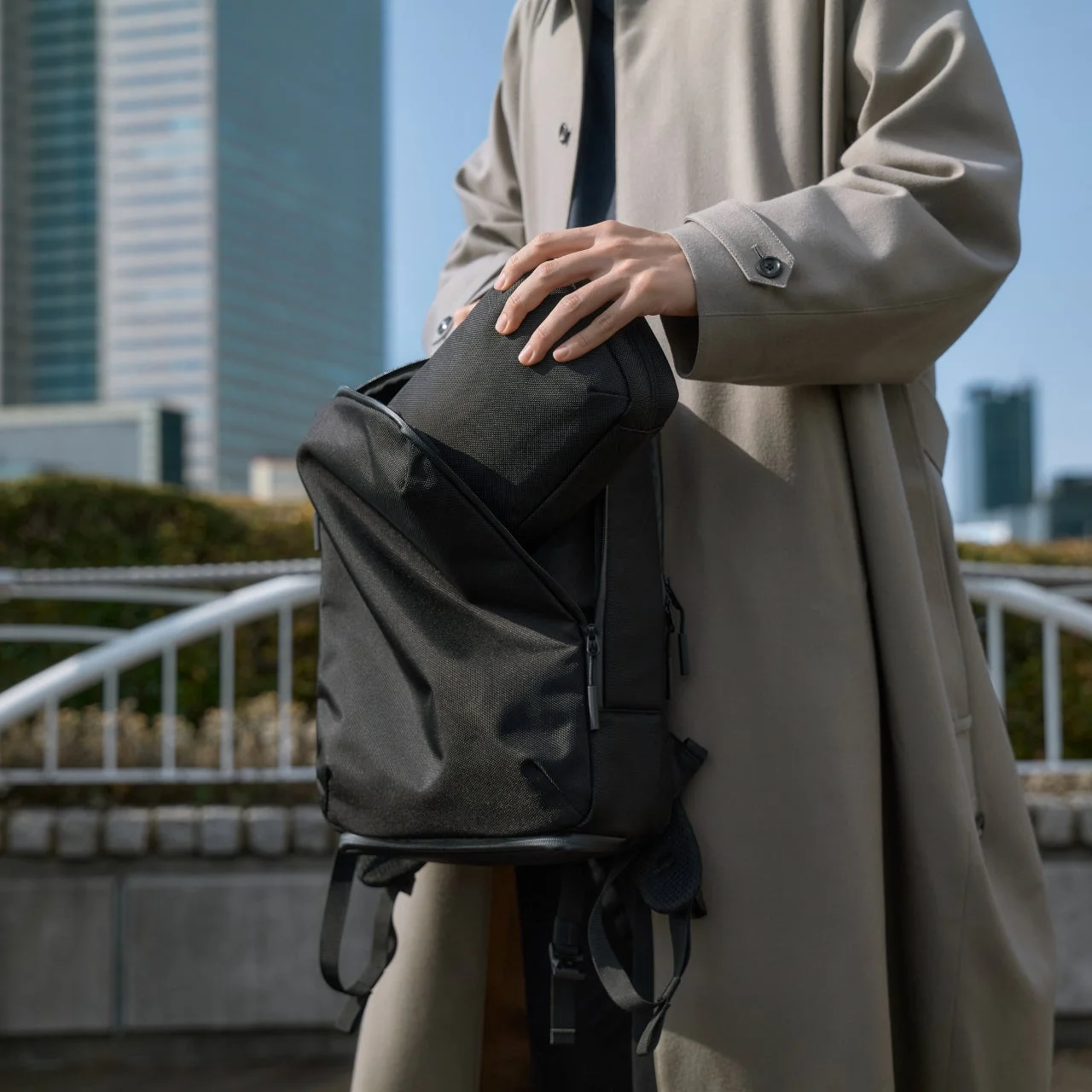 トレンチコートを着た人物がリュックにポーチを収納する様子