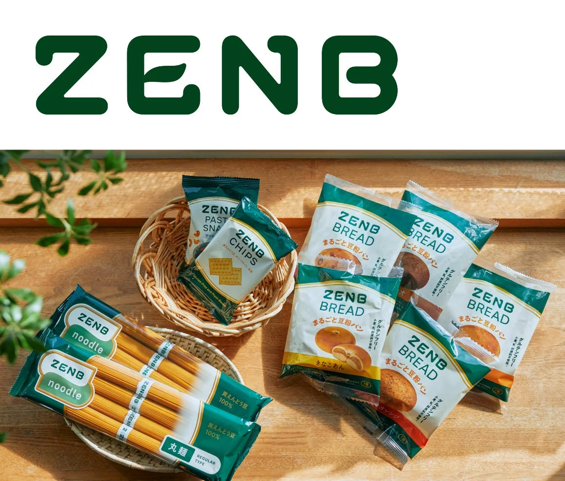 ZENBブランドの様々な食品が木製のテーブルに並べられています。パスタ、パン、チップス、スナックがあり、健康志向の製品であることが伺えます。