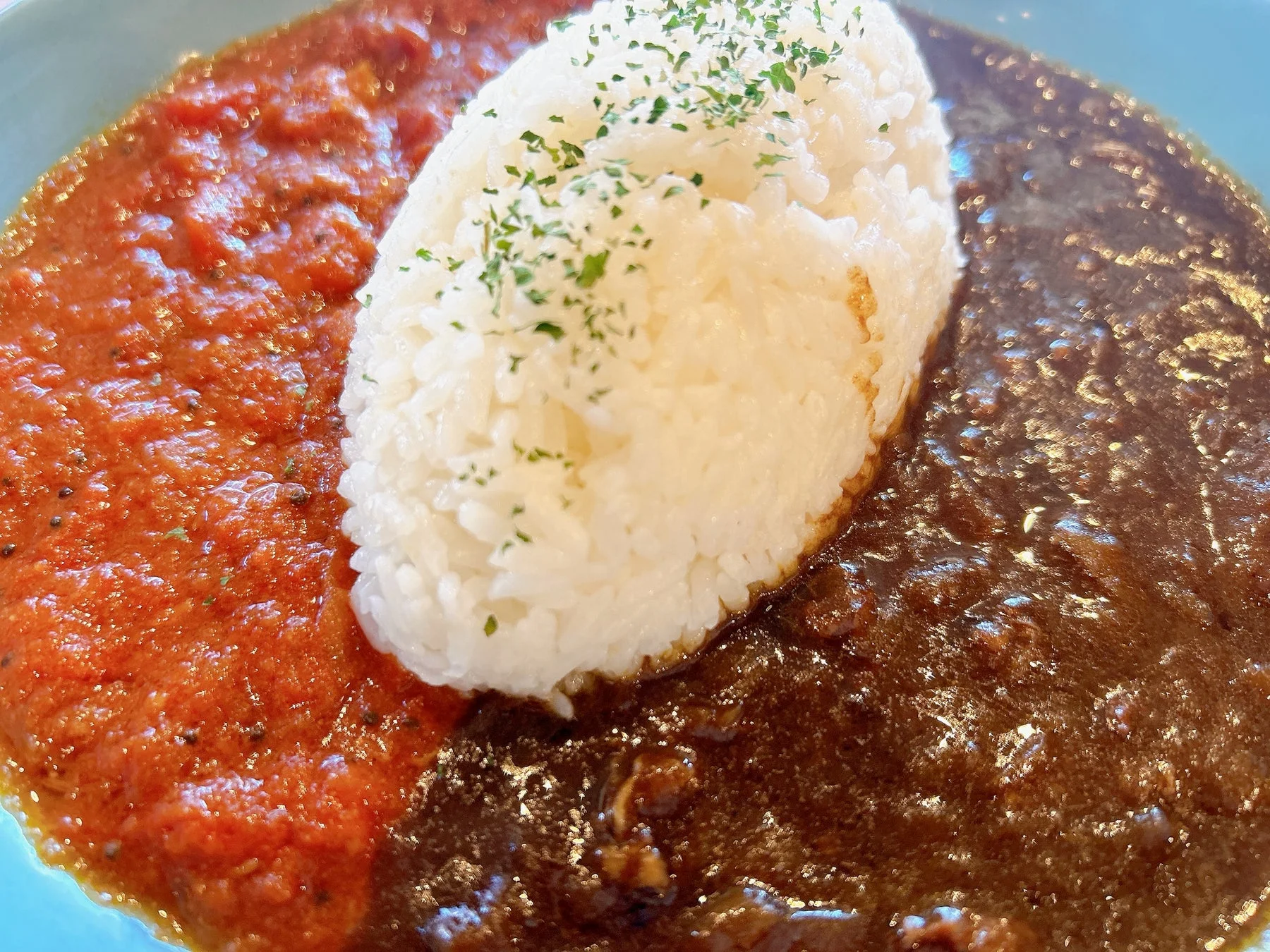 白いご飯が中央に盛られ、片側に赤色のトマトソース、もう片側に濃い茶色のカレーソースが添えられた合がけカレー
