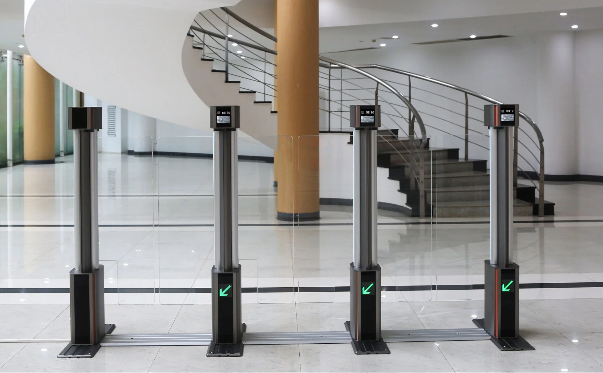 現代的な建物のエントランスに設置された複数の入退場ゲートシステム。各ゲートには時刻表示と緑色の矢印があり、奥には螺旋階段が見える。