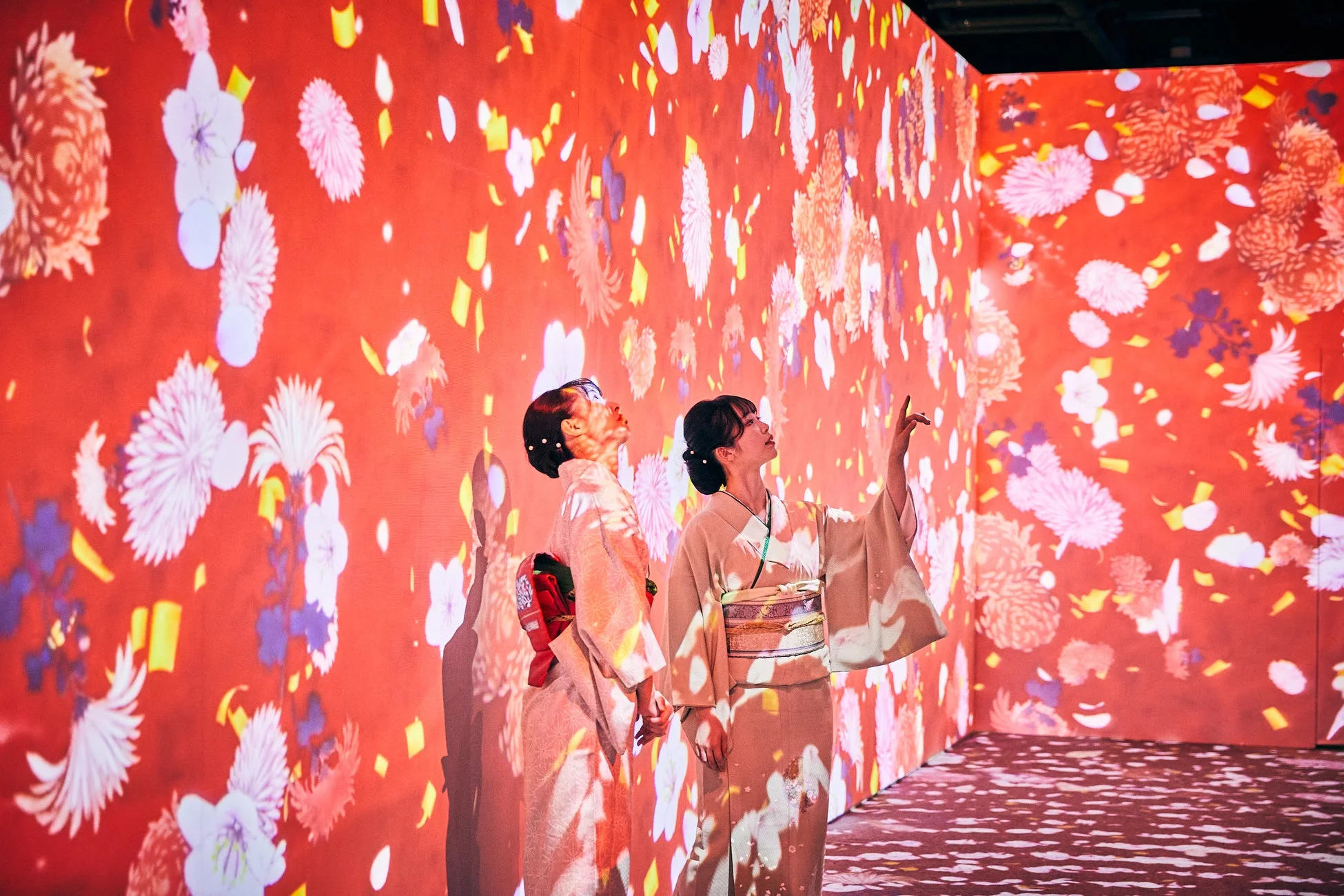 赤い花が舞うデジタルアートを楽しむ着物姿の女性たち