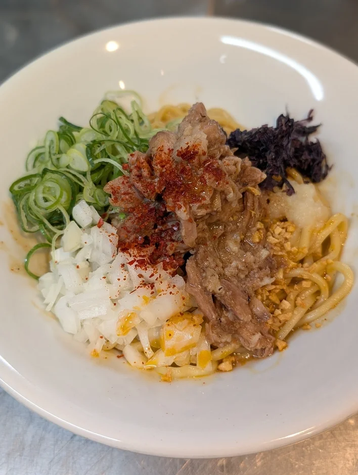 ほぐし豚肉、刻みネギ、刻み玉ねぎ、唐辛子などがトッピングされたまぜそば