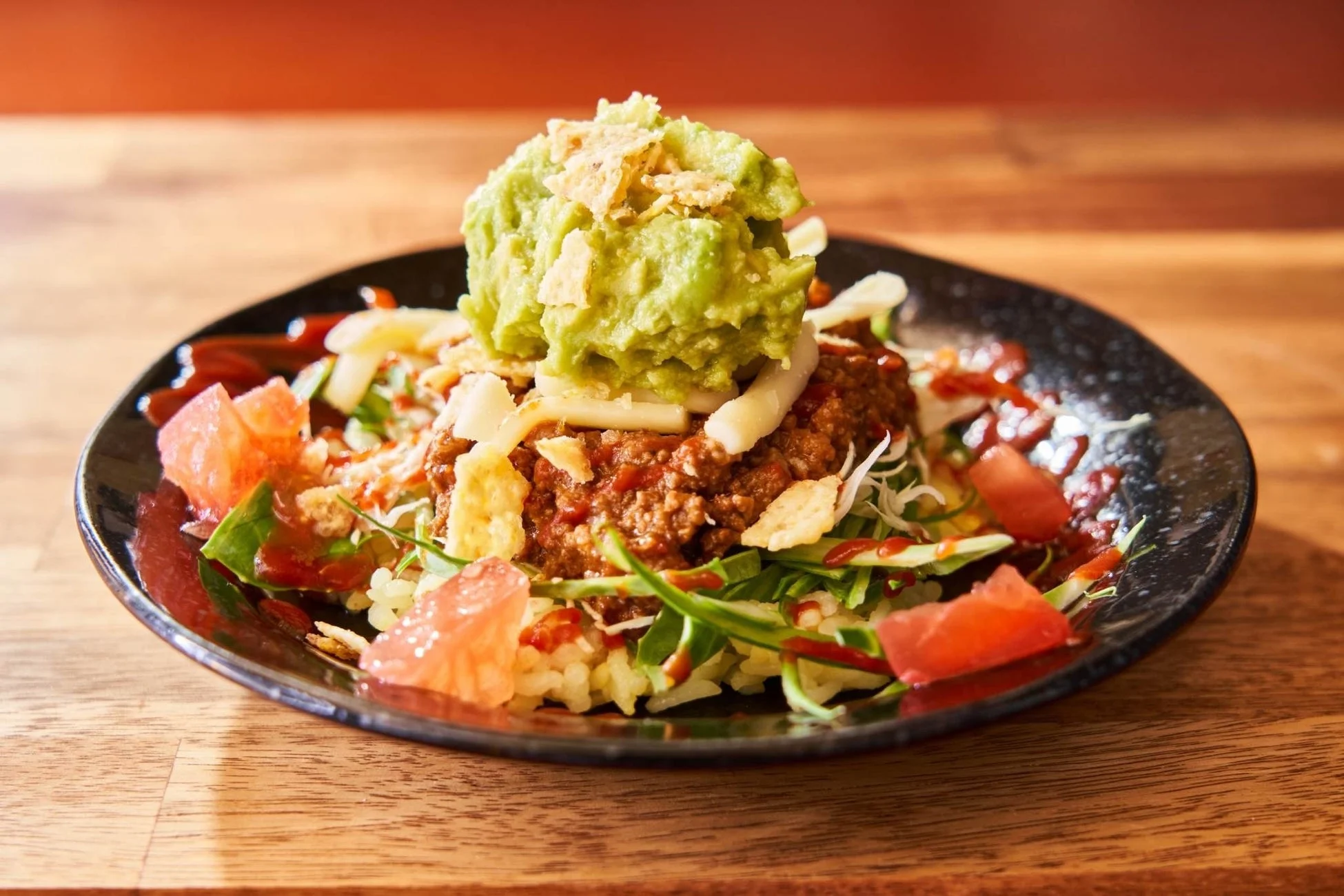 ご飯の上にタコミート、レタス、チーズ、トマトが盛り付けられ、中央には大きなアボカドがたっぷりと乗った彩り豊かなボウル料理