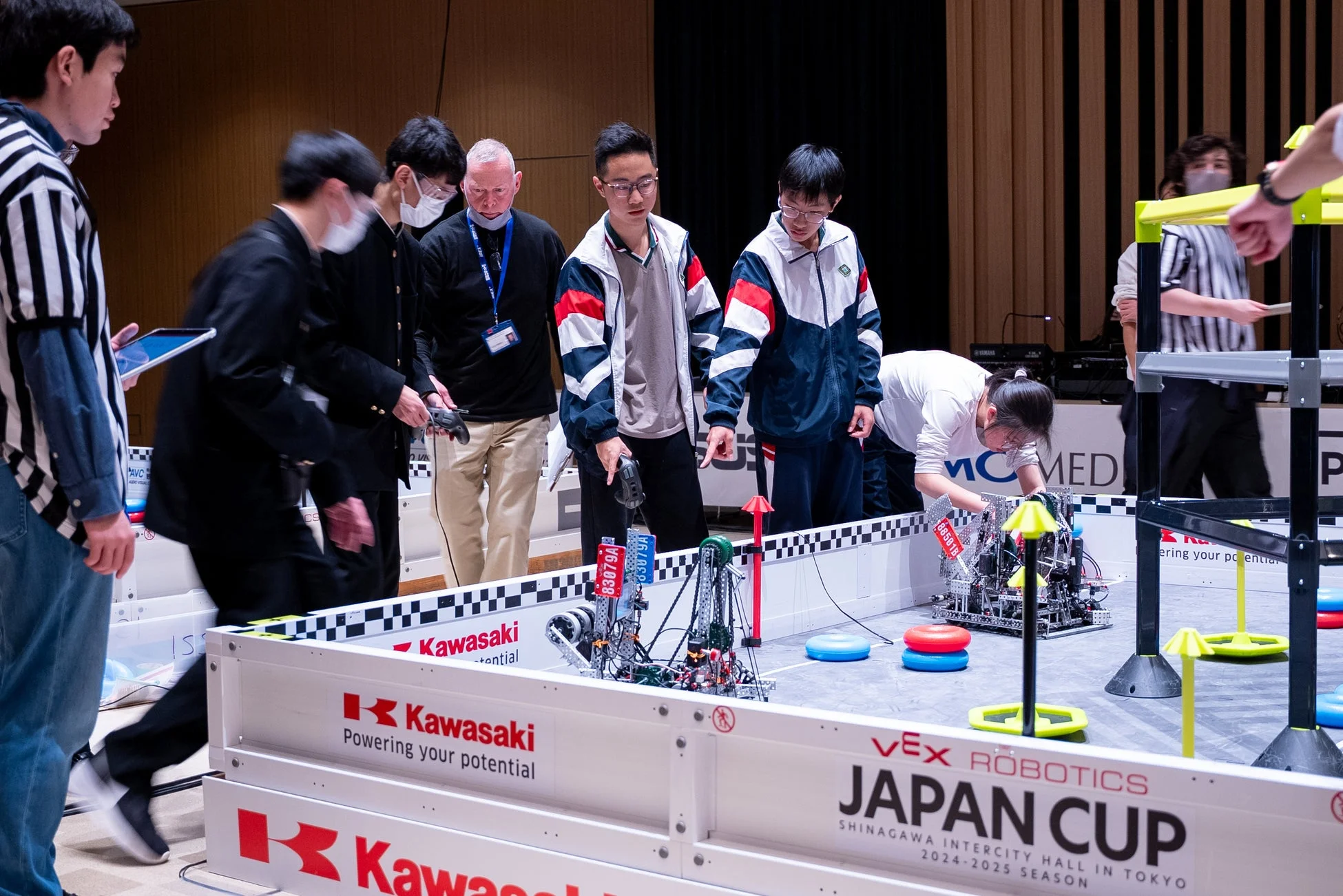 VEXロボティクス・ジャパンカップで、複数の参加者がロボットを操作し、競技フィールドで真剣に活動している様子です。