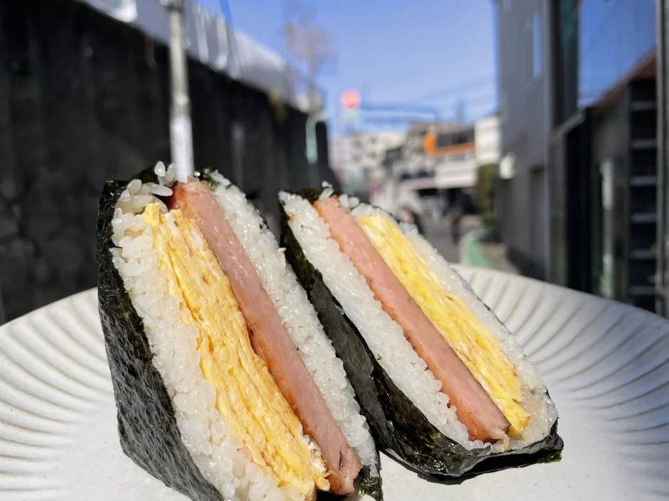 青空の下、白い皿に盛り付けられたスパムおにぎり2個