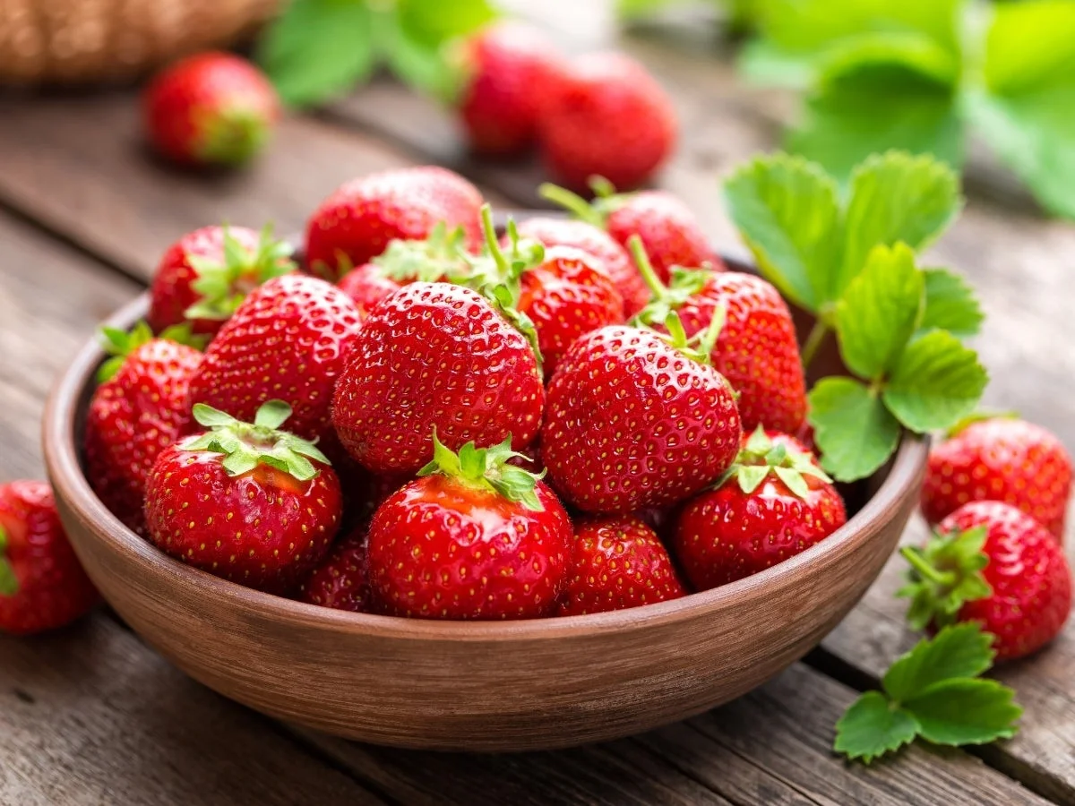 木製のテーブルに置かれた茶色のボウルに、鮮やかで熟した赤いイチゴが山盛りに盛られています
