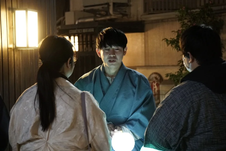 和服の男性が光る球体を持って他の2人と話している夜の情景