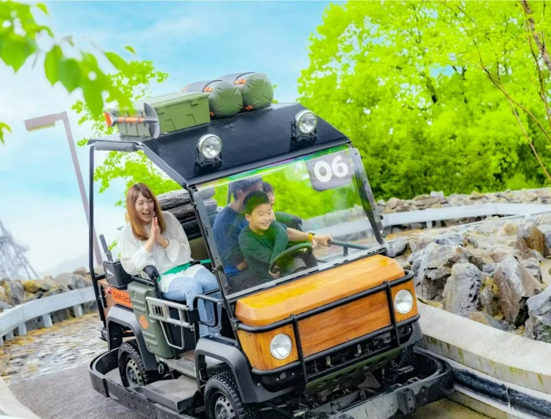 家族がオフロード風の乗り物に乗って楽しんでいる様子。子供が運転するサファリ風のアトラクションで、皆が笑顔を見せています。緑豊かな屋外で、楽しいひとときを過ごしているようです。