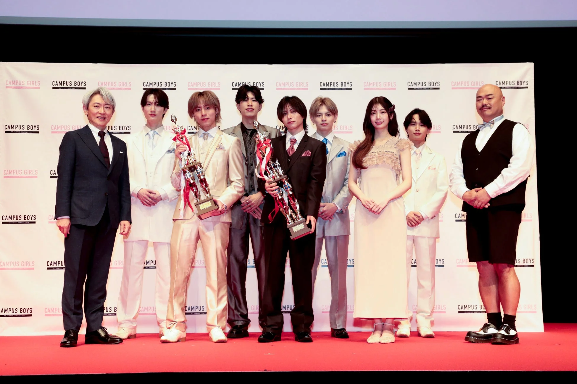 赤いカーペットの上で、男女がトロフィーを持って並んでいるイベントの集合写真です。背景には「CAMPUS GIRLS」や「CAMPUS BOYS」のロゴがあり、コンテストの表彰式の様子を捉えています。