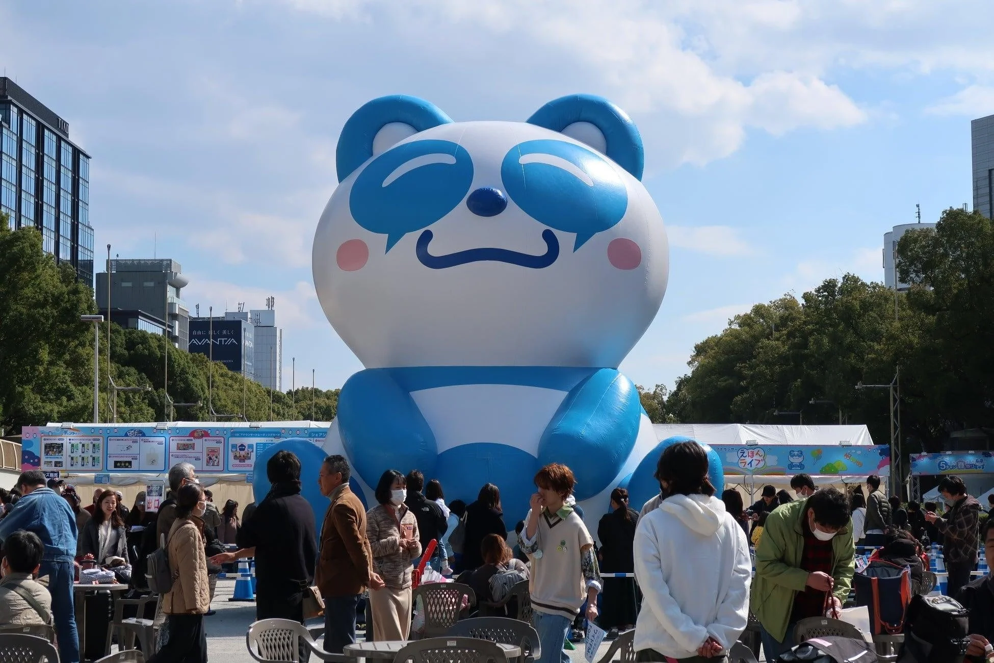 青と白の巨大なパンダ型バルーンが設置された屋外イベント会場で、多くの人々が集まっている様子