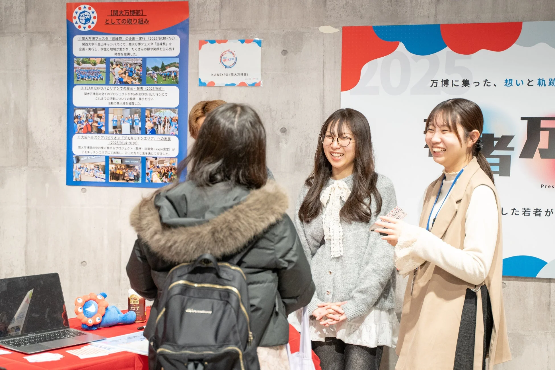 万博関連のイベントブースで、若い女性たちが笑顔で交流している様子