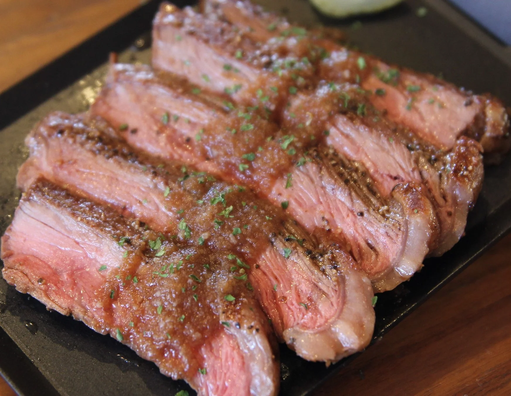 ミディアムレアに焼かれたステーキが、ソースとハーブで飾られ、黒いプレートに盛り付けられた画像