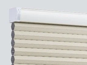 ベージュ色のハニカムシェードのクローズアップ画像です。折りたたまれたプリーツ状の生地と白いヘッドレールが特徴で、窓辺のインテリアとして機能性とデザイン性を兼ね備えています。