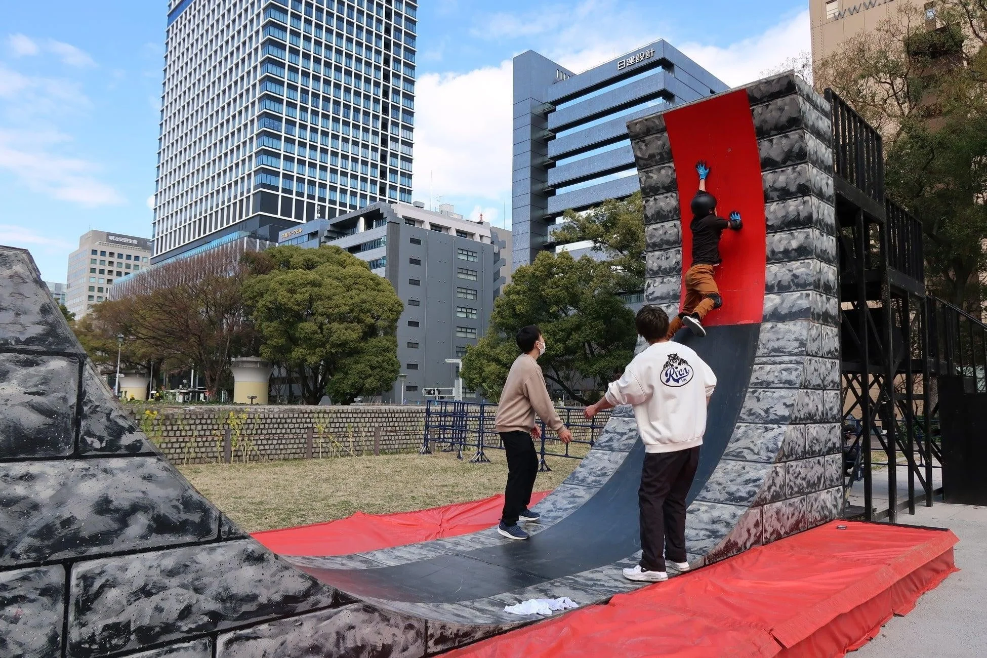 都市公園で子供が傾斜のある赤いボルダリングウォールを登っている
