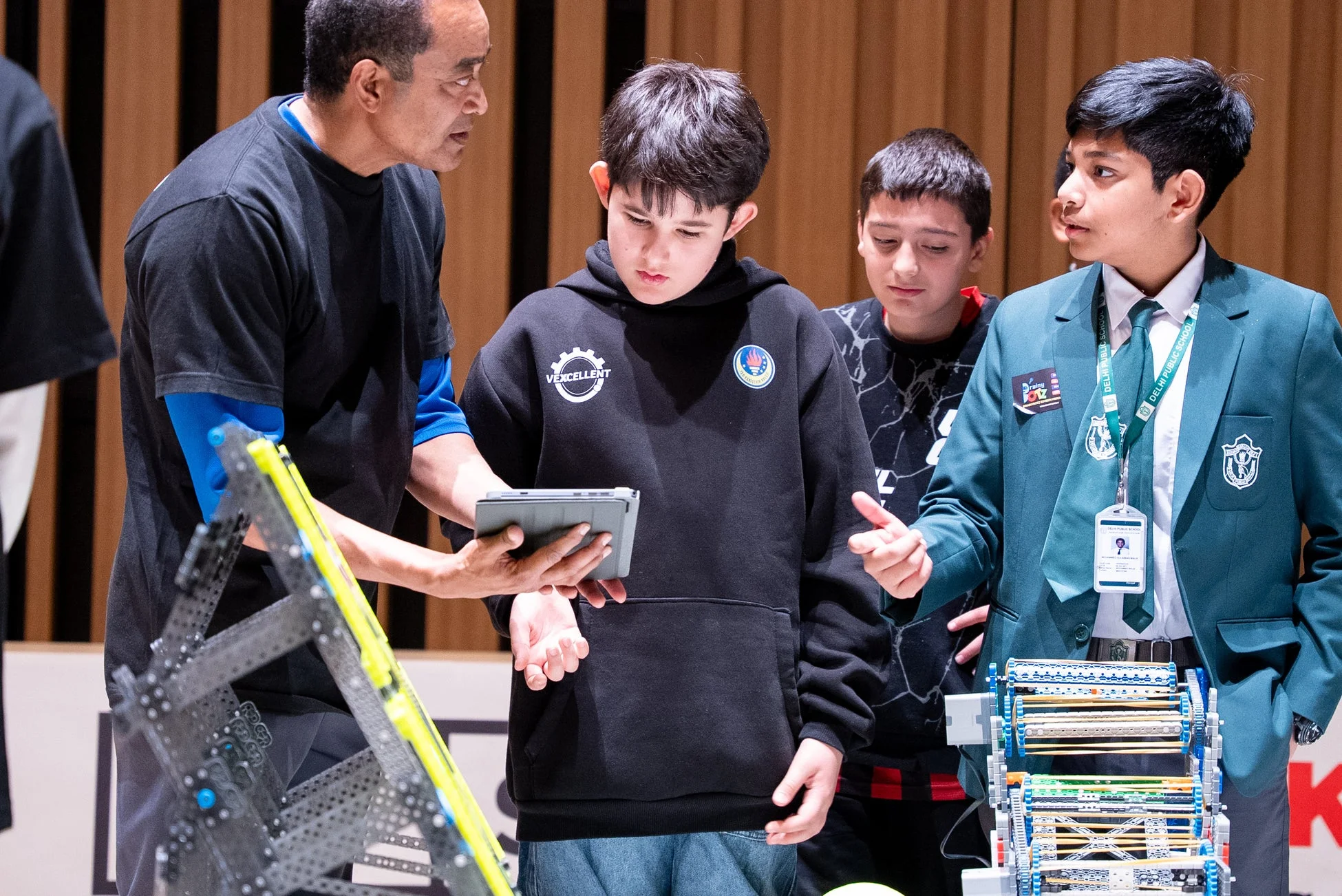 ロボット競技会で、大人が子供たちにタブレットを使ってロボットについて説明している様子。