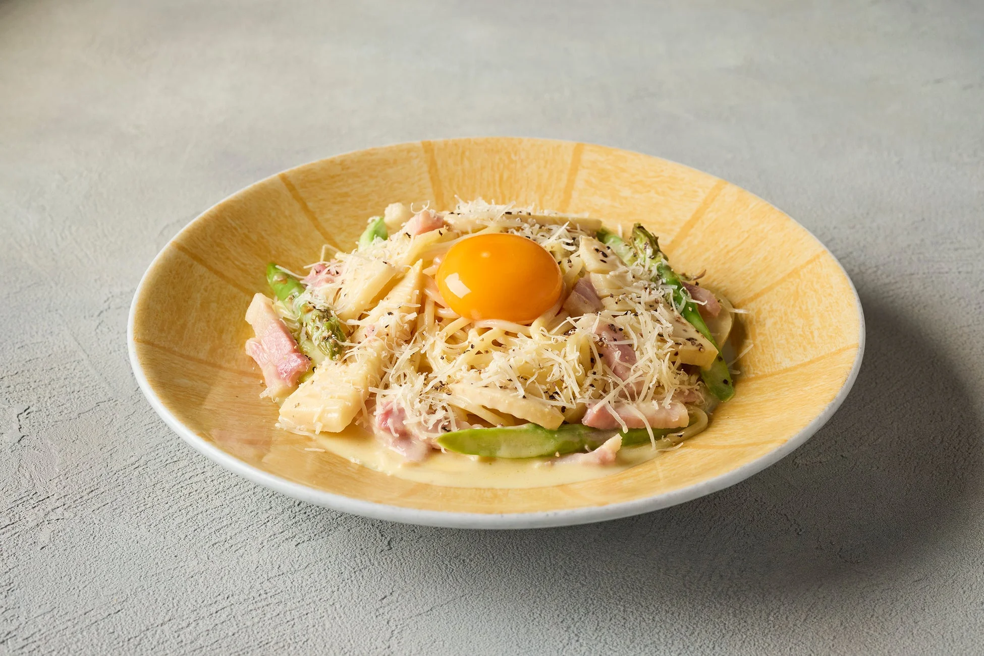 卵黄、ベーコン、アスパラガス、たけのこが盛り付けられたクリーミーなパスタ料理