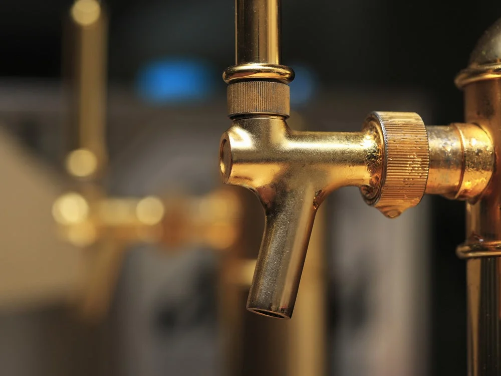 金色の蛇口がクローズアップで捉えられており、先端から水滴が垂れている様子