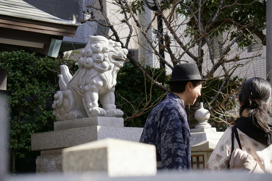 神社の狛犬の傍らを和服姿の男性が歩く風景