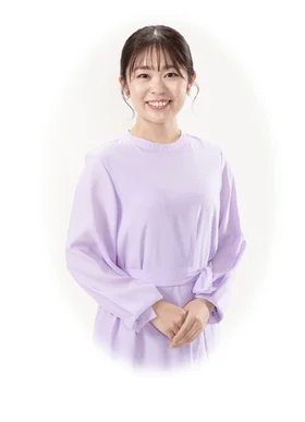 薄紫色の服を着て、穏やかな笑顔を浮かべ、両手を体の前で組む若い日本人女性