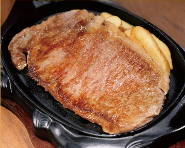 熱々の鉄板に盛り付けられた、香ばしく焼き上げられたステーキとフライドポテト