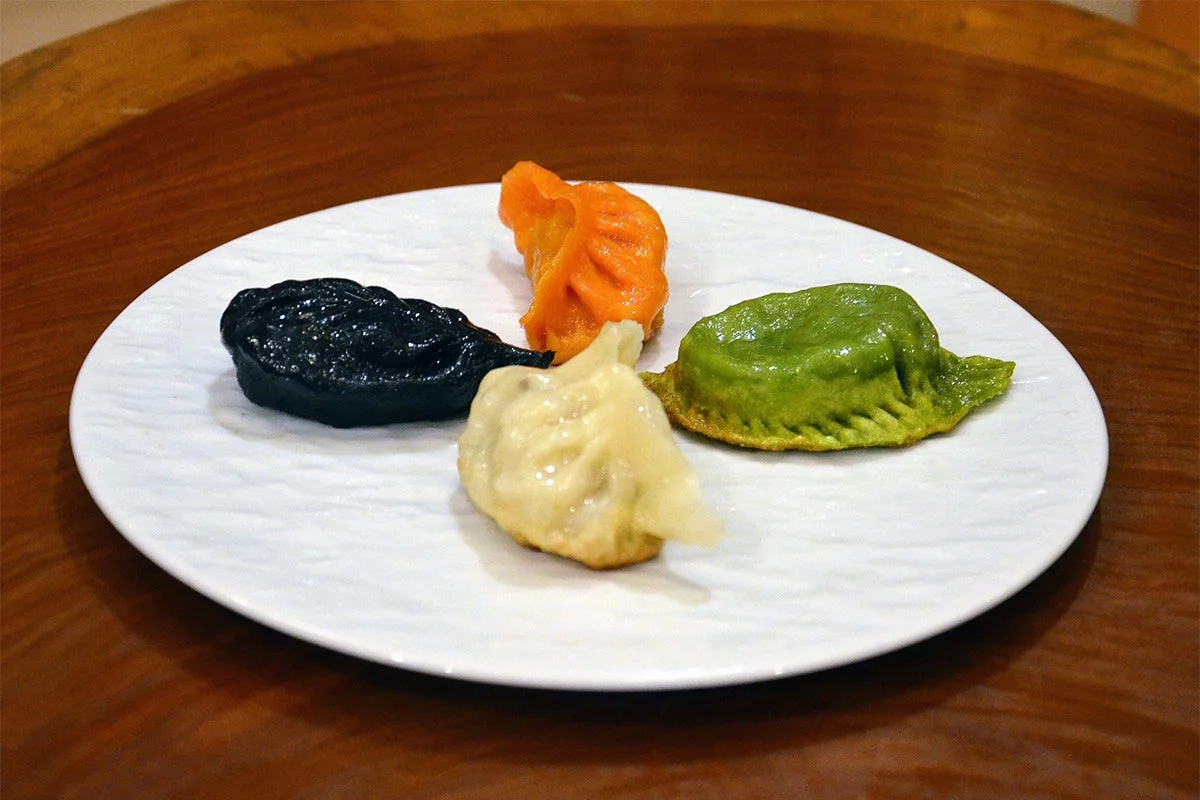 白い皿に盛られた、黒、オレンジ、白、緑の4種類のカラフルな餃子（点心）のアップ写真