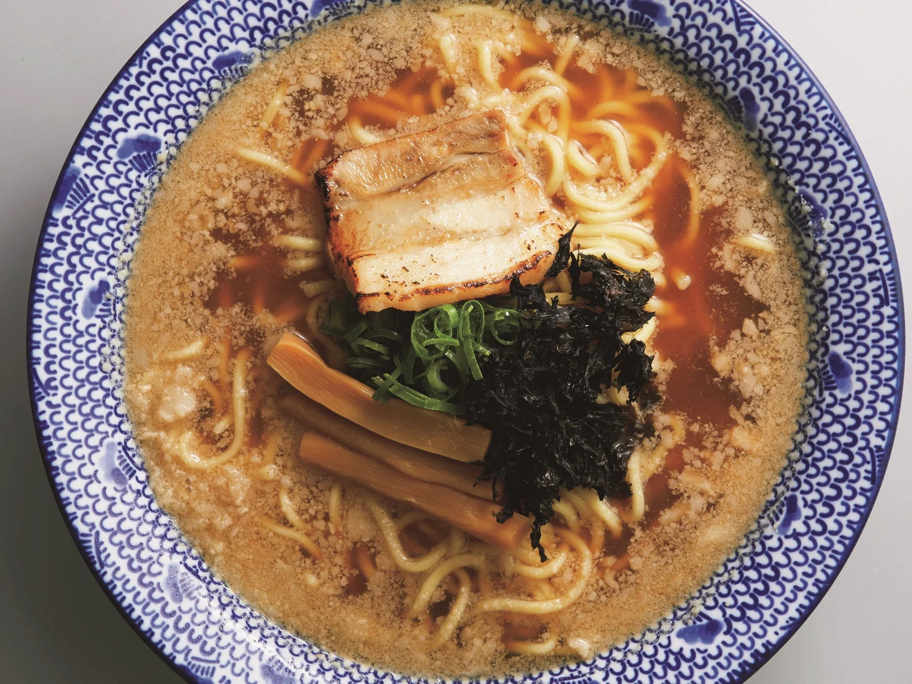 とろみのあるスープに麺が絡むラーメンのクローズアップ。炙りチャーシュー、ネギ、メンマ、海苔がトッピングされ、青と白の美しいどんぶりに盛り付けられています。食欲をそそる一杯です。
