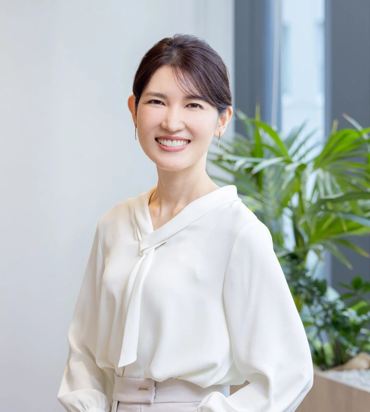 白いブラウスを着た女性が、明るい室内で笑顔を見せているポートレート写真