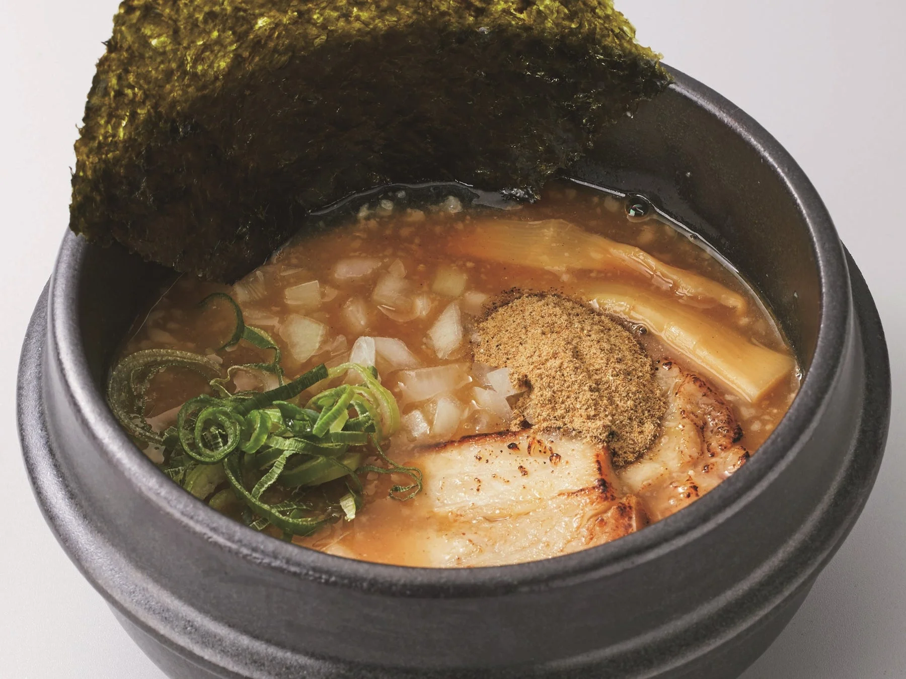黒い器に盛り付けられた、海苔、チャーシュー、メンマ、ネギ、玉ねぎ、そして魚粉らしきトッピングが特徴の濃厚なスープのラーメン。食欲をそそる一品です。