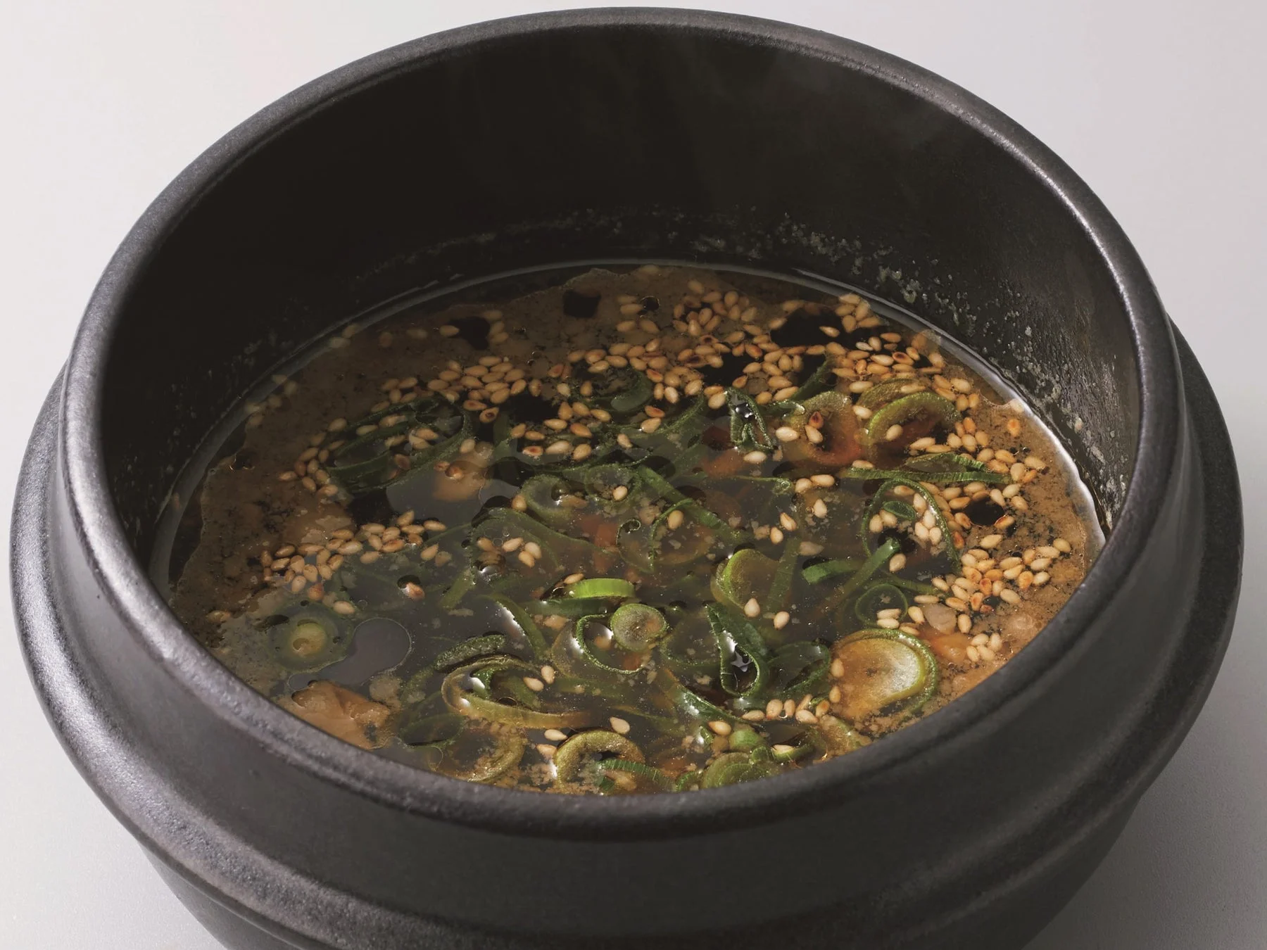 黒い石鍋に盛られた、刻みネギと白ごまがたっぷり入った温かい汁物です。香ばしい香りが漂うアジアンテイストの一品で、食欲をそそります。