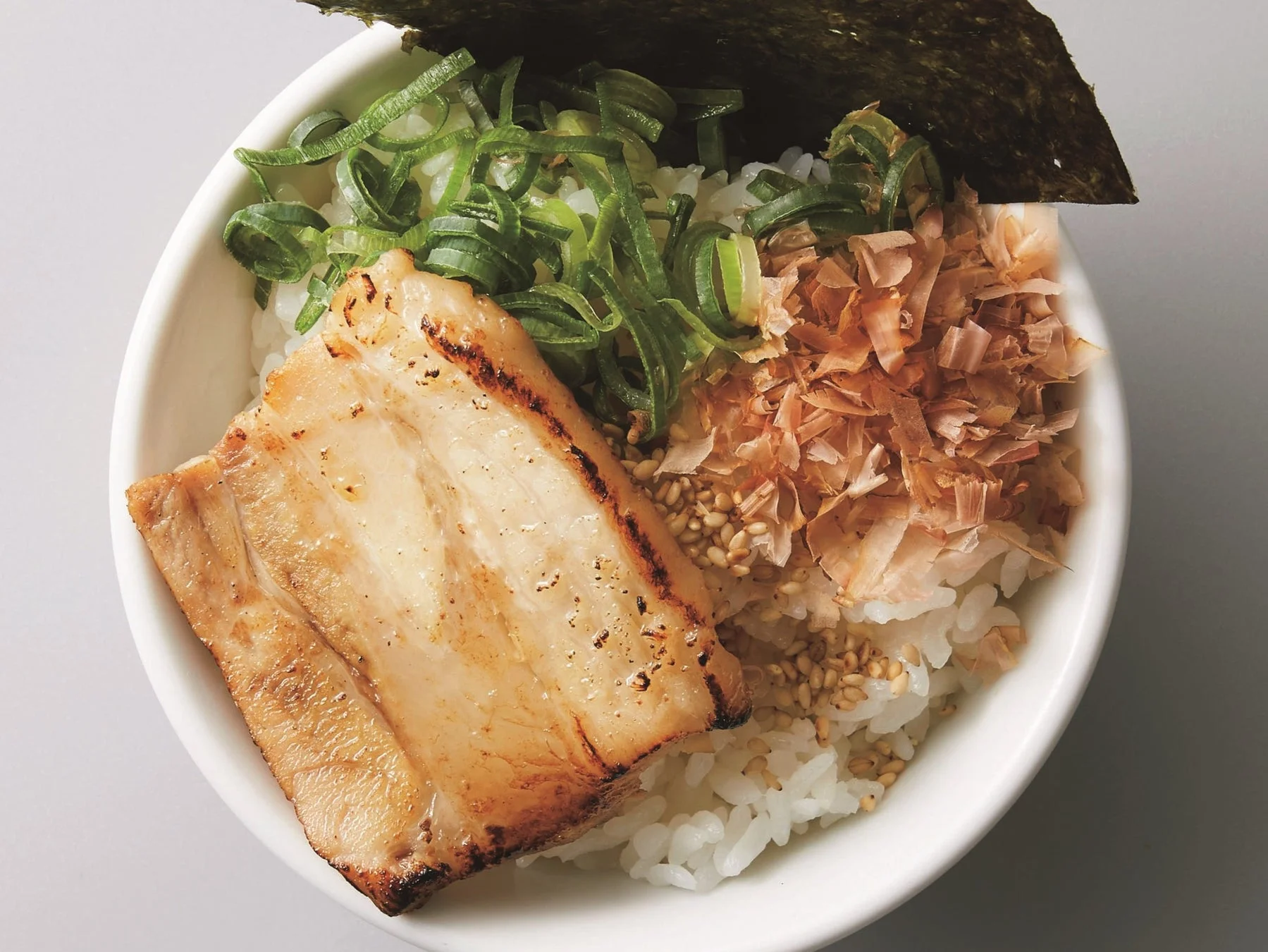 香ばしく焼かれた豚肉が乗ったご飯に、刻みネギ、鰹節、胡麻、海苔が添えられた食欲をそそる丼です。日本の家庭料理や定食屋でよく見られる一品です。