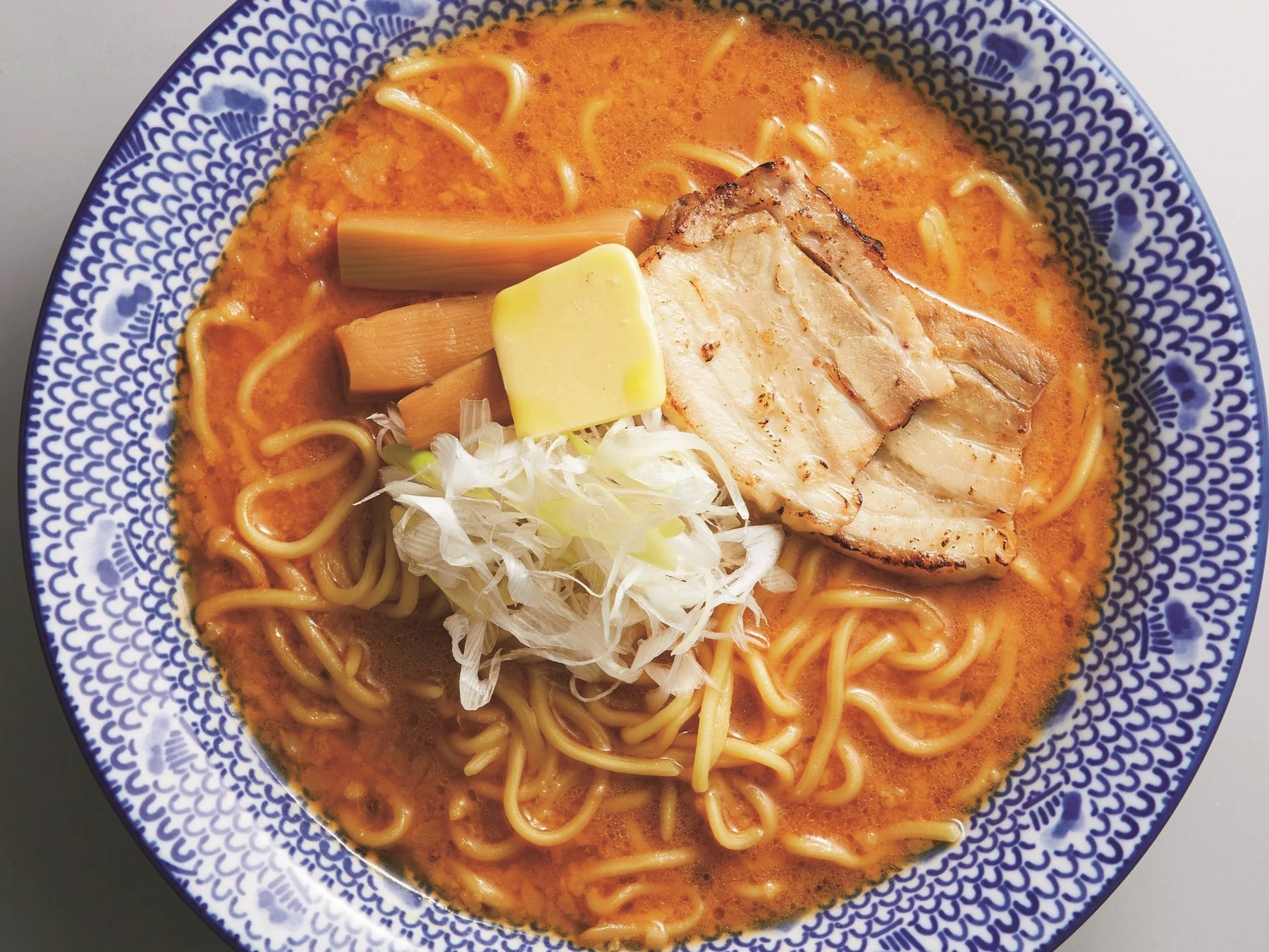 赤みがかった濃厚なスープに麺が絡み、チャーシュー、バター、メンマ、白髪ネギがトッピングされた味噌ラーメンのクローズアップ写真です。