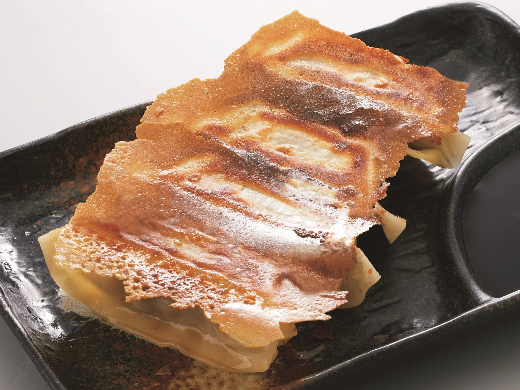 香ばしく焼き上げられた羽根つき餃子が黒い皿に盛り付けられています。パリッとした食感の羽根が特徴で、隣にはタレを入れるくぼみがあります。