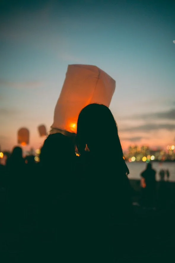 夕暮れにランタンを放つ人々