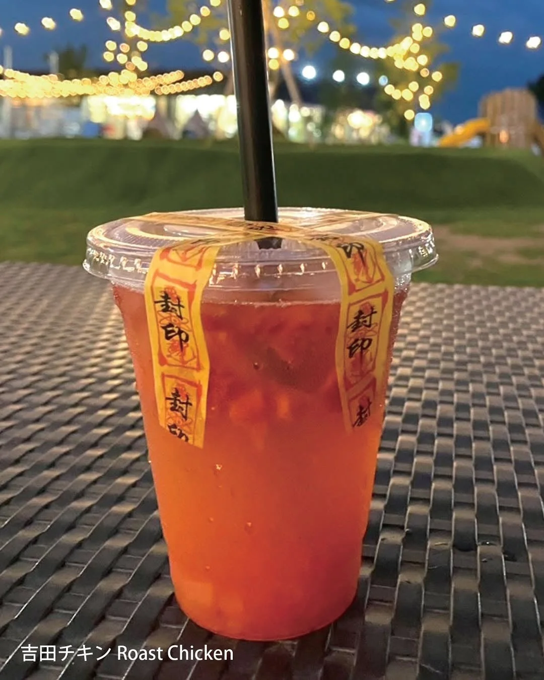 夜の屋外でテーブルに置かれた、オレンジ色の飲み物が入ったプラスチックカップ