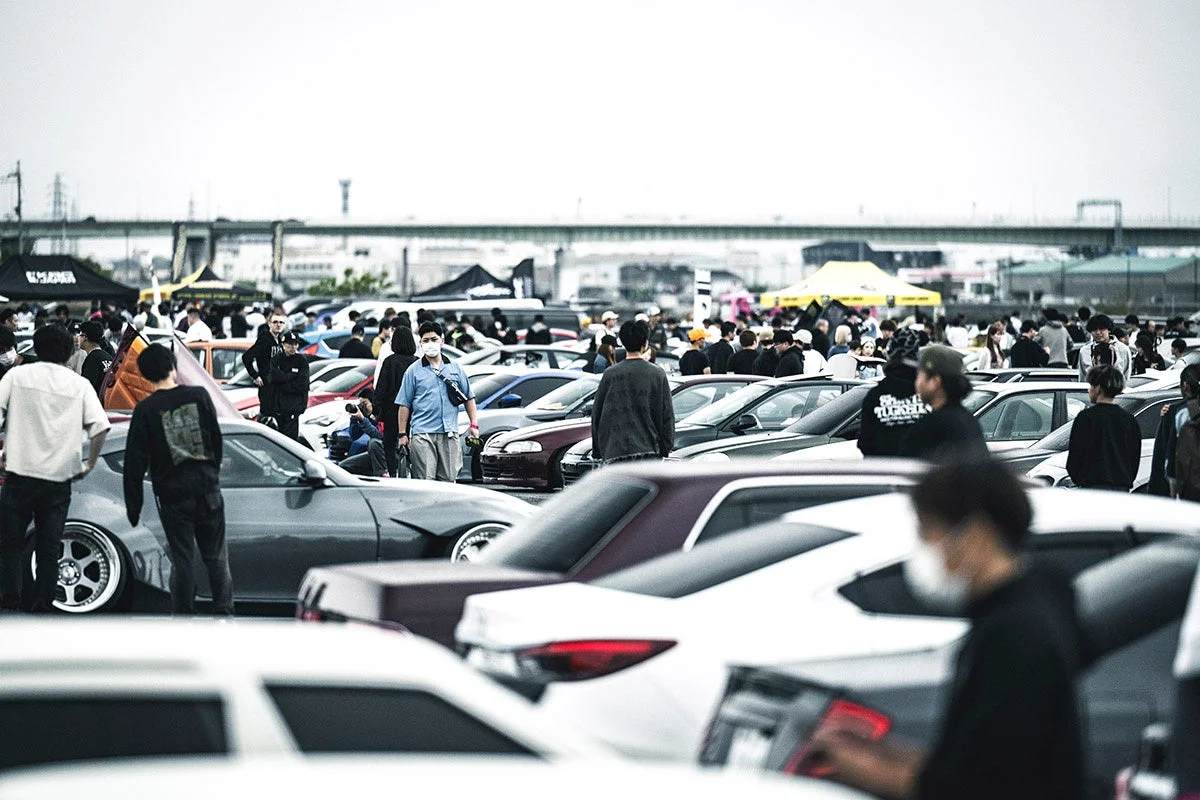 多くのカスタムカーと人々が集まる屋外のカーイベントの様子