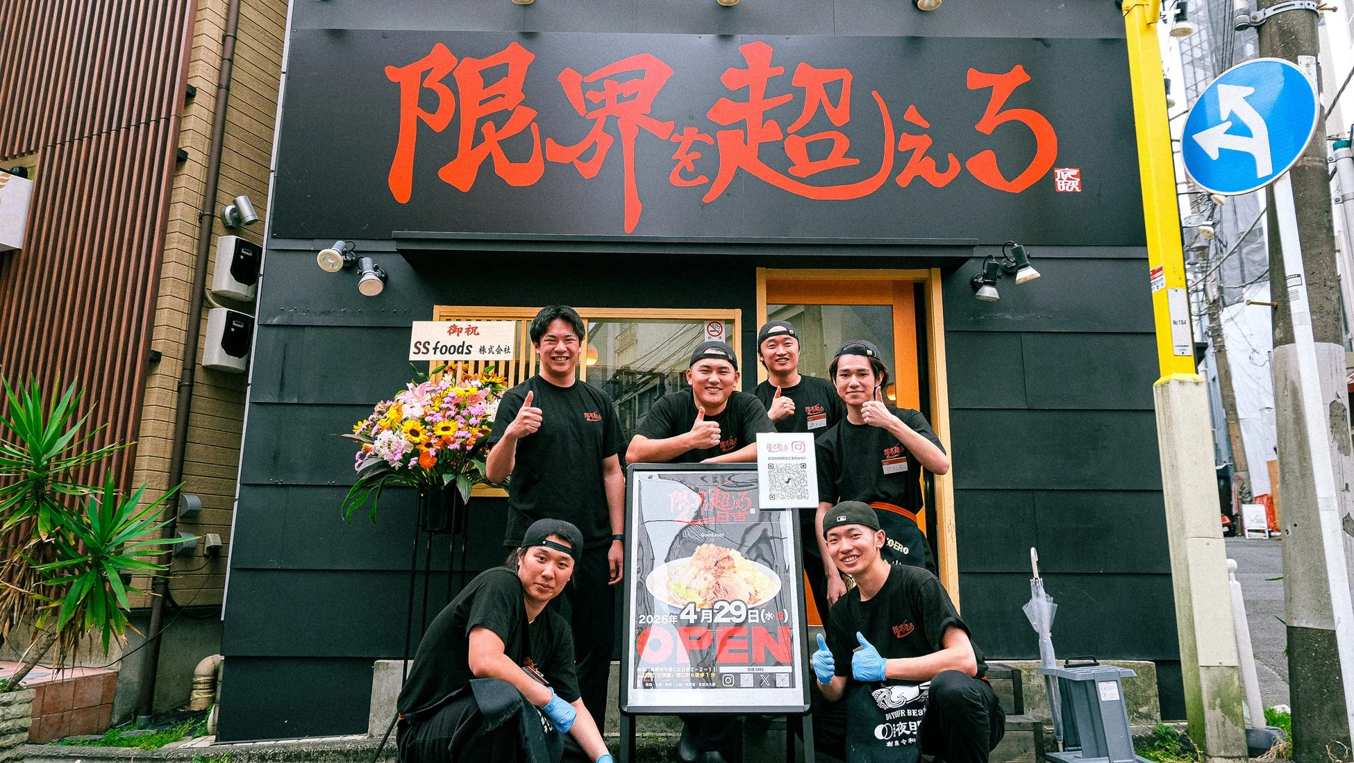 「限界を超えろ」という店名のラーメン店の前に立つ、開店を祝う店員たちの写真