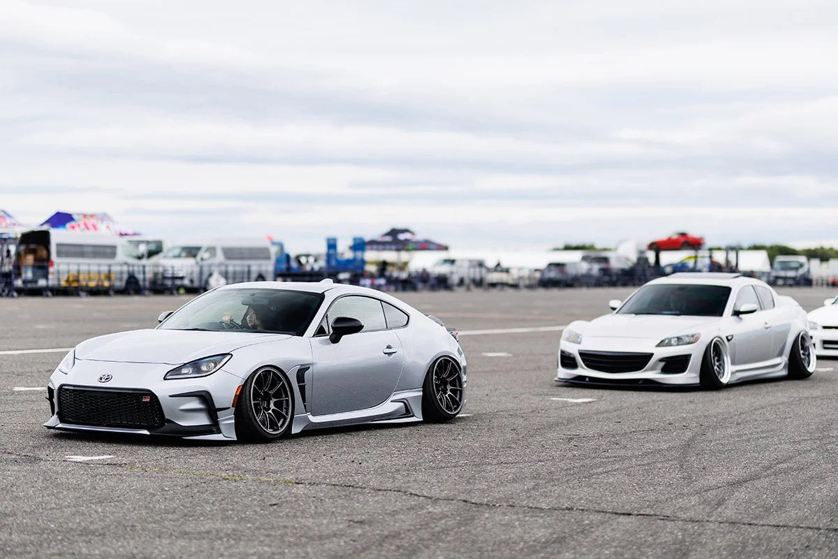 低い車高にカスタムされたシルバーのトヨタGR86とマツダRX-8が舗装された広場に並んでいます